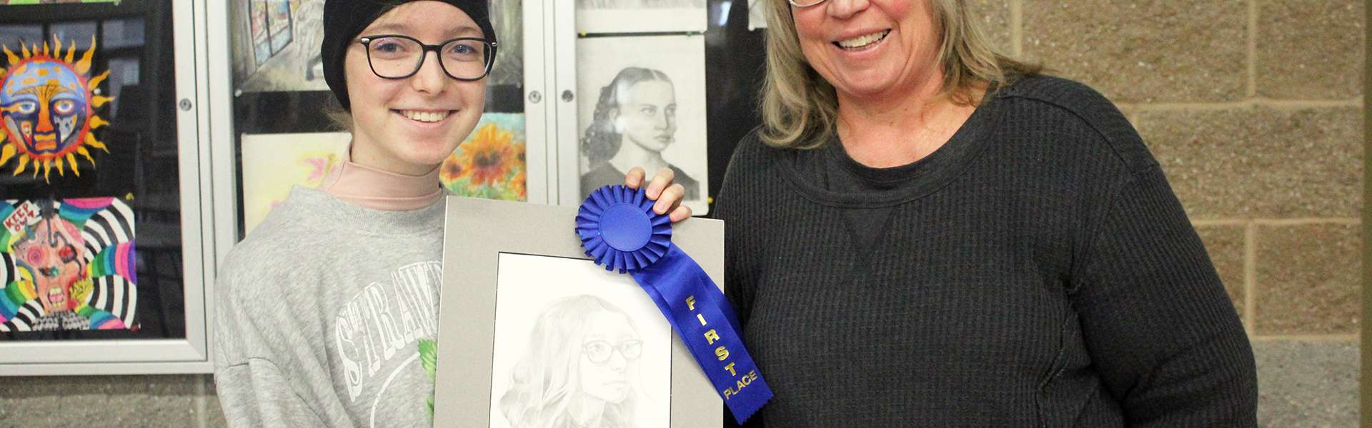 Sophie Paulsen (left) and Ms. Tami Aufderheide pose with Sophie's first place drawing, ribbon, and prize on Monday, Feb. 24. | Photo by Hayley Daniels