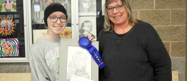 Sophie Paulsen (left) and Ms. Tami Aufderheide pose with Sophie's first place drawing, ribbon, and prize on Monday, Feb. 24. | Photo by Hayley Daniels